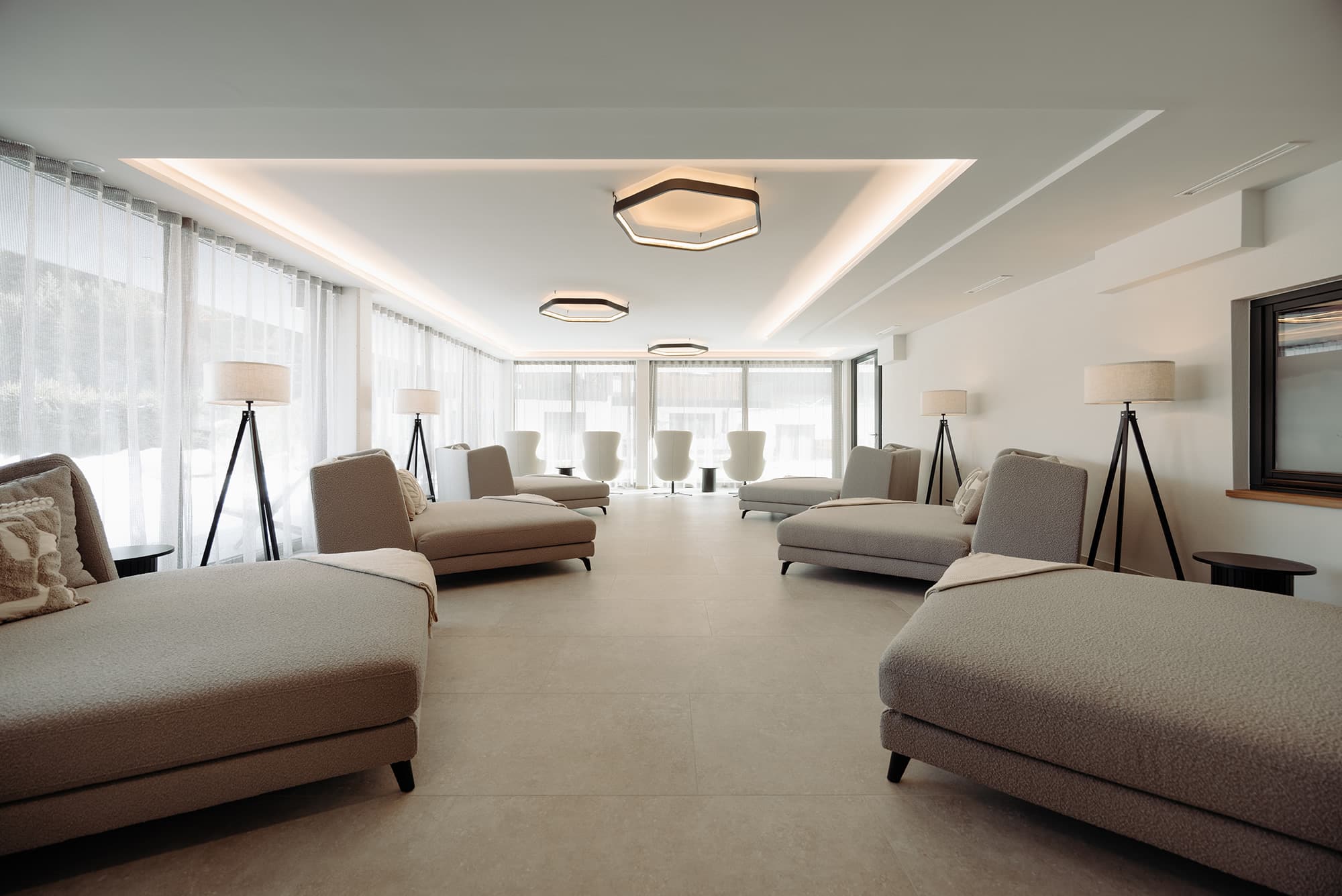 Moderner Ruheraum mit Lounge-Bereich mit grauen Sofas, Stehlampen und großen Fensterfronten im Wellnesshotel loj in Flachau